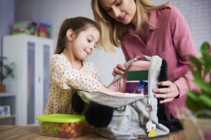 Young mum and daughter packing backpack for the school; back to school tips for parents