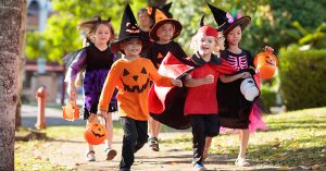 Child in Halloween costume. Mixed race Asian and Caucasian kids and parents trick or treat on street. Little boy and girl with pumpkin lantern and candy bucket. Baby in witch hat. Autumn holiday fun; blog: dos and don'ts of trick or treating