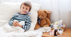 Sick child boy lying in bed with a fever, resting at home; blog: Sick Days: When to Keep Your Child Home From School
