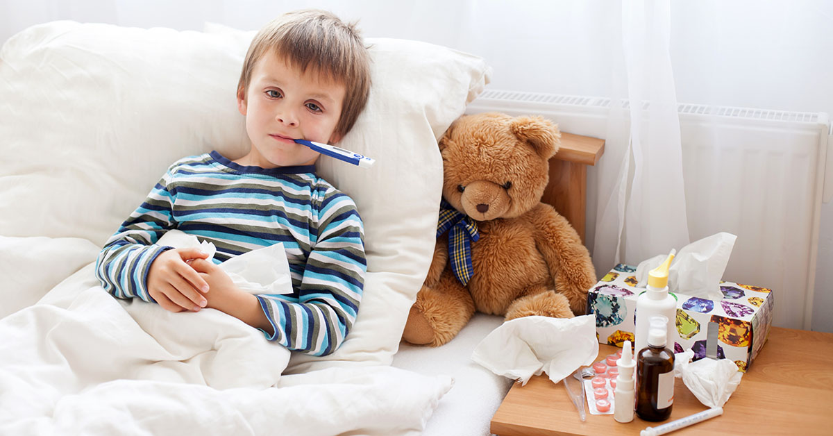 Sick child boy lying in bed with a fever, resting at home; blog: Sick Days: When to Keep Your Child Home From School