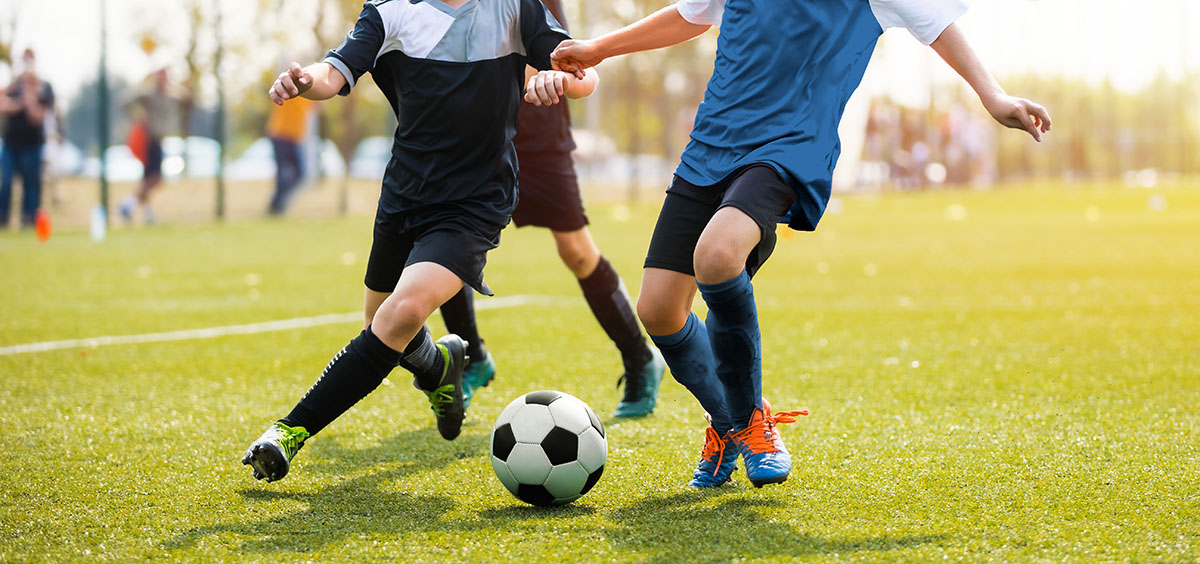 Two soccer players running and kicking a soccer ball. Legs of two young football players on a match. European football youth player legs in action; blog: Preventing and Treating Common Kids Sports Injuries