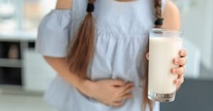 Little girl with dairy allergy holding glass of milk indoors; blog: 8 Most Common Food Allergies in Kids