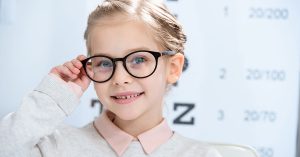 adorable smiling child looking at camera in glasses at oculist consulting room; blog: Does Your Child Need Glasses?