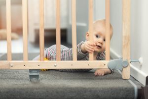 child playing behind safety gates in front of stairs at home