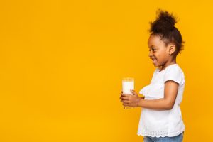 Adorable little african girl holding glass with fresh milk