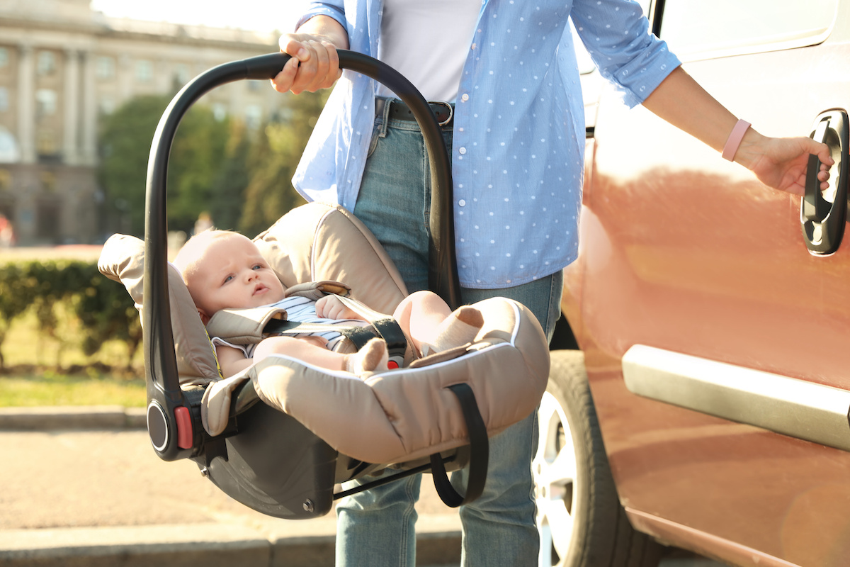Mother holding child safety seat with baby near car outdoors / blog - bringing home your baby